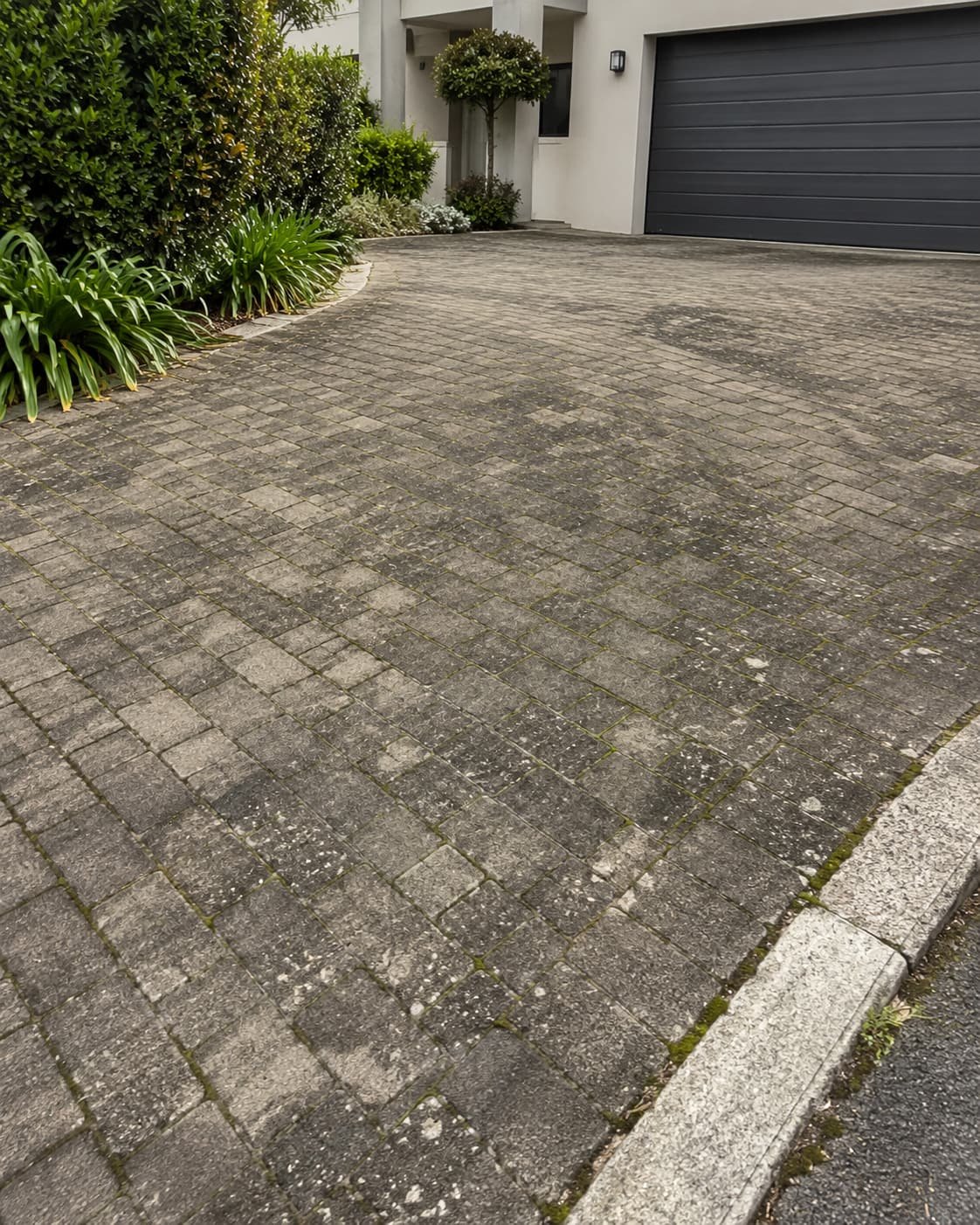 Block-paved driveway stained with grime and moss before cleaning